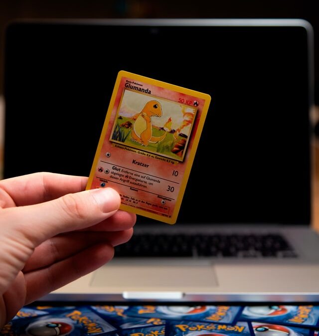 A hand holding up a Glumanda Pokemon card. The rest of the deck of Pokemon cards are face-down sprawled out on the table.