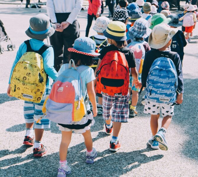 A crowd of young children with colorful backpacks and hats travel together.
