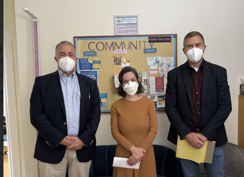 Dr. Mel Houser, Executive Director of All Brains Belong VT poses with John Lyon and Jon Valsangiacomo,, Trustees of the Melissa Andrews Trust. Behind them is a bulletin board reading: COMMUNITY. They all wear N95 masks to protect from transmission of COVID19